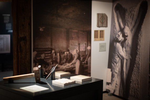 Ausschnitt aus dem Ausstellungsraum &quot;Marmor I&quot; mit der Taststation zum Erleben der unterschiedlich gemeiselten Steinobeflächen vor großflächigen Impressionen aus der Marmorsteinverarbeitungswerkstatt.