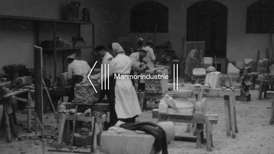 Schwarz-Weiß-Foto von Marmorarbeitern, die den Stein in einer traditionellen Werkstatthalle bearbeiten.